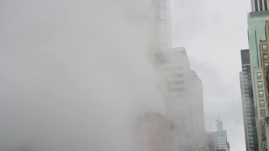 A chimney with steam with buildings in the background
