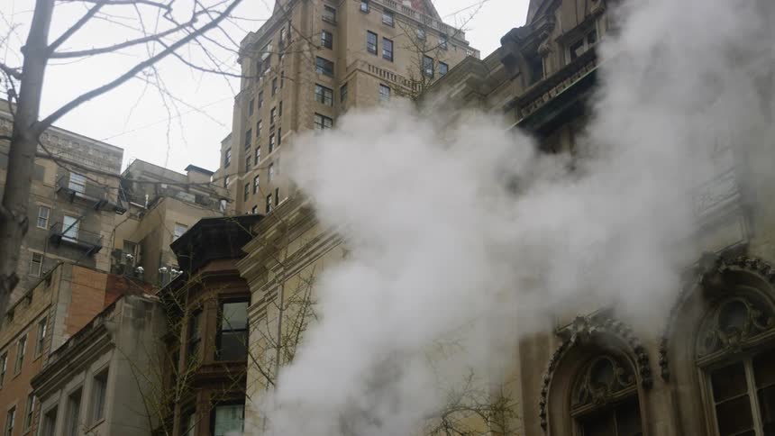 Steam rises up from the city street and billows in front of buildings