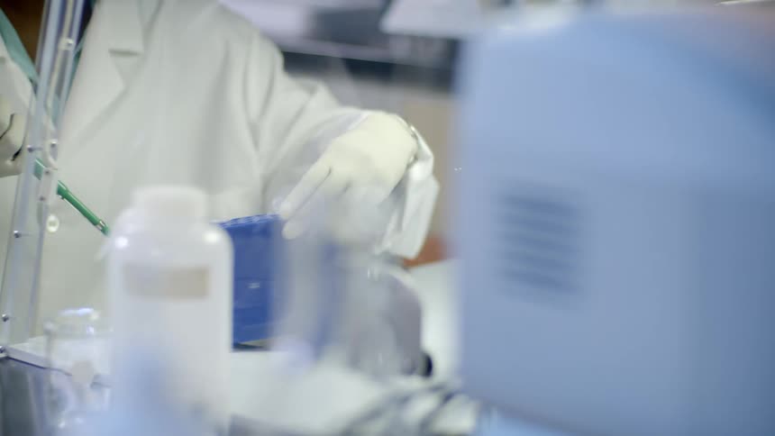 A scientist in a lab inserts liquid into a test tube in a blue case then moves it