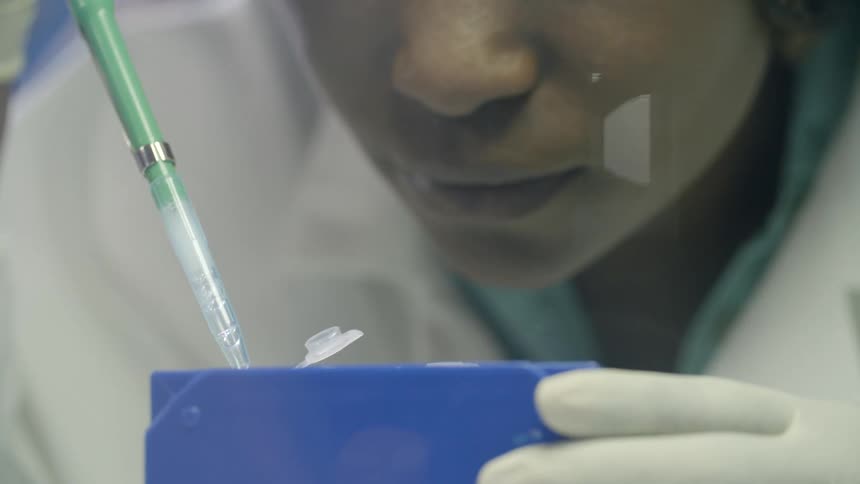 Technician in lab coat adds liquid to container with a dropper