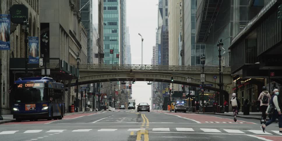 Vehicles and pedestrians bustle along street passing under a bridge downtown
