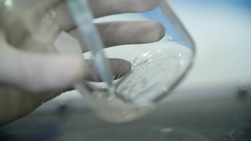 A lab technician is putting liquid in a jar