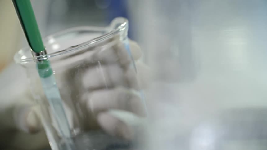 A person wearing gloves using a dropper to get liquid from a beaker