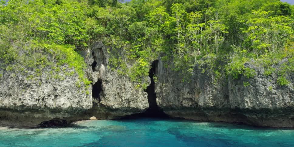 Crystal clear water flowing towards caves in the side of very steep seaside cliffs