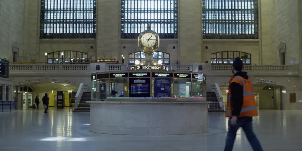 A worker in an orange vest walks through an almost deserted grand central station