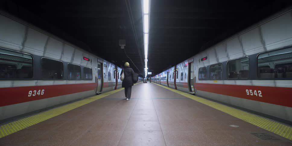 A woman walks on a platform between two trains in a station
