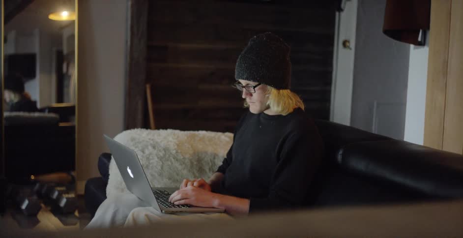 A man sits on the couch typing on his laptop