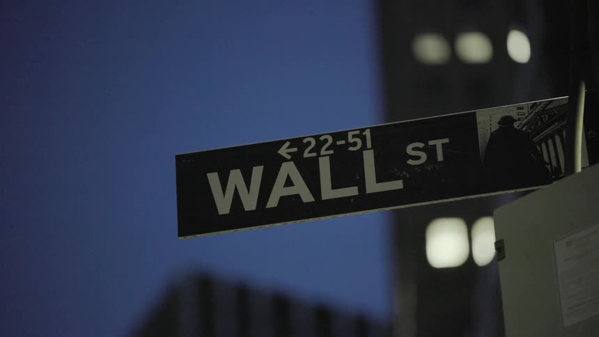 Lights in skyscraper windows glow behind a wall st street sign