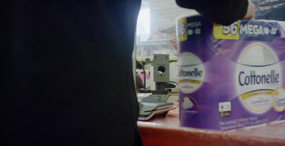 A person in a store buying toilet paper while the cashier is behind plastic and has on a mask