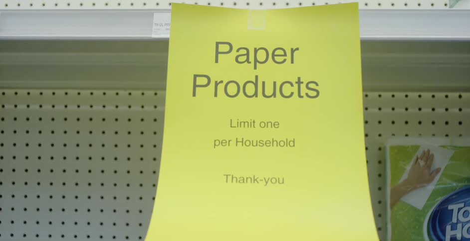 A paper sign is taped to an empty grocery store shelf limiting paper products to one per household