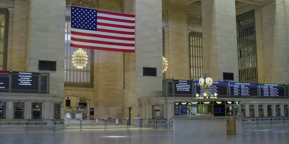 An american flag hangs between columns in an empty grand central station terminal