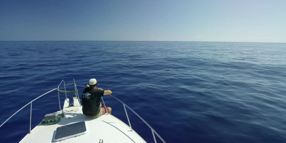 A man sits on the front of a boat in the ocean on a sunny day