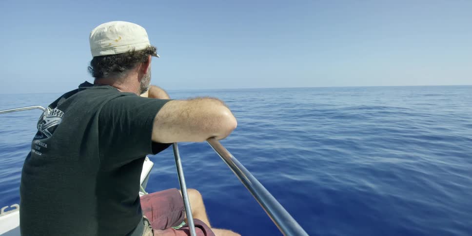 A man sits on the bow of a boat at sea