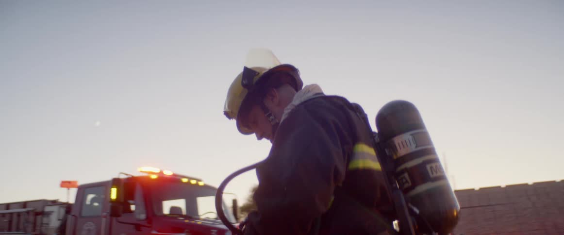 A fireman in full gear walks toward a building and away from a fire