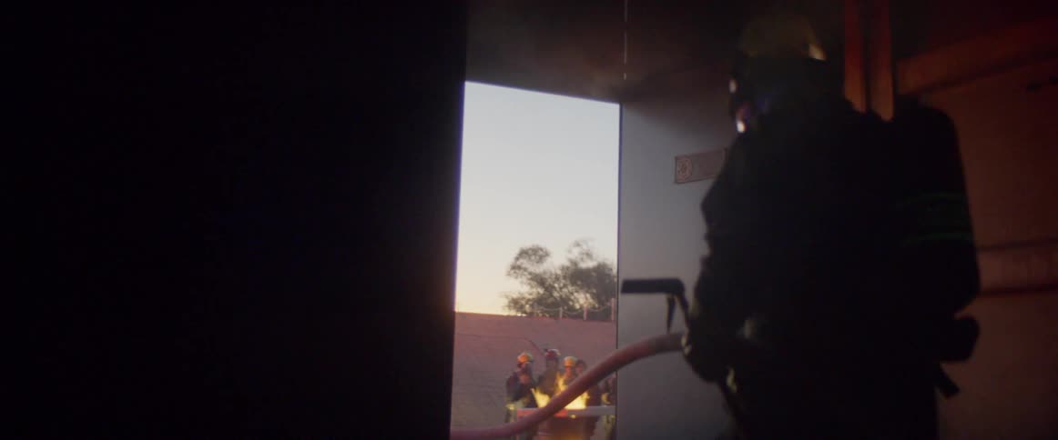 Firefighters leave a house and walk toward a fire outdoors