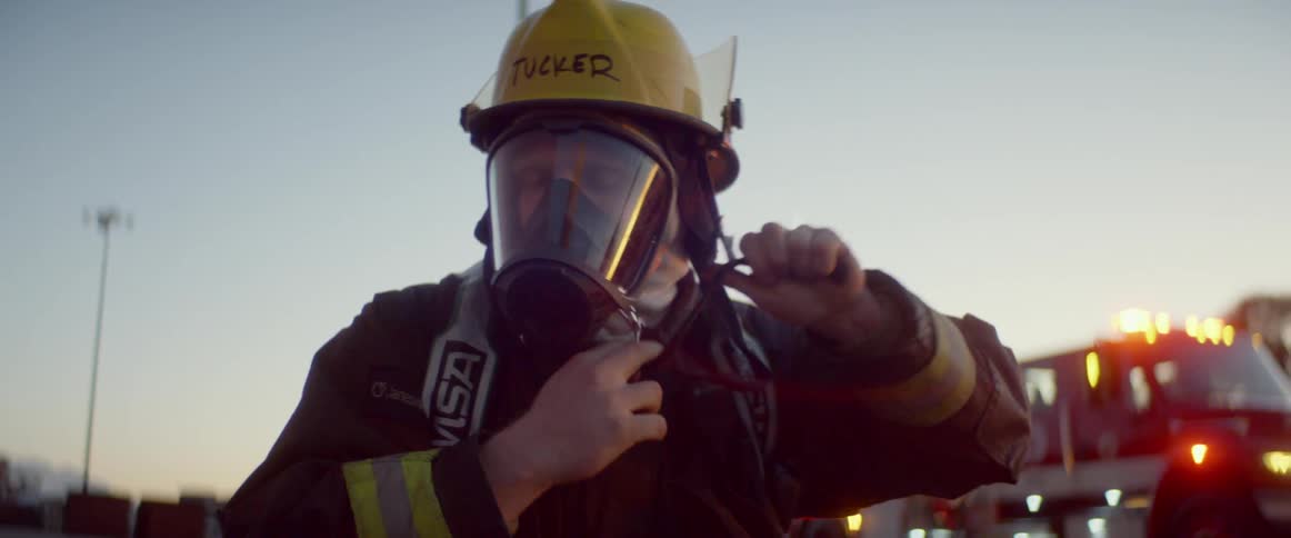 Firefighter dons protective gear near building as fire engine waits
