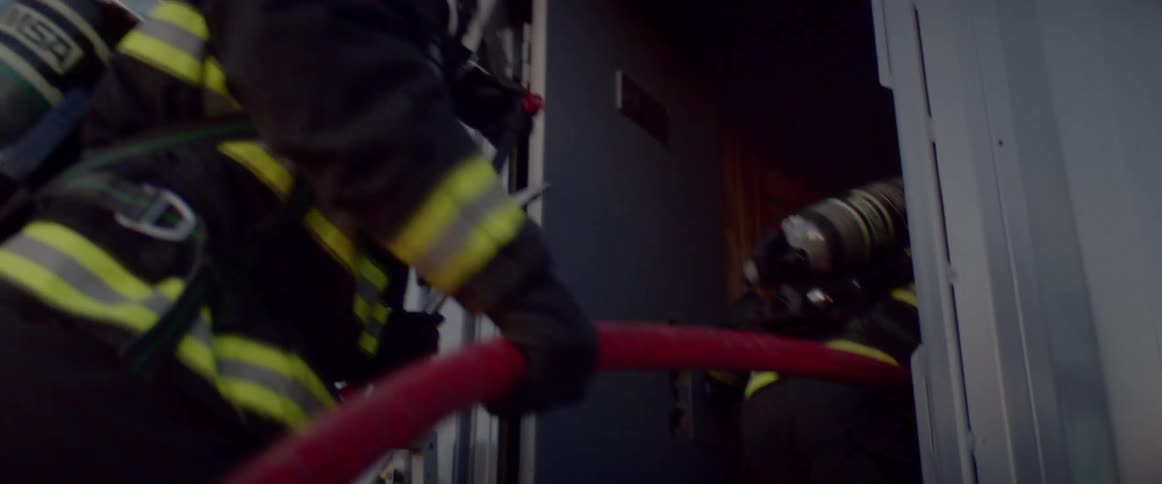 Firefighters enter building carrying hose at sunset
