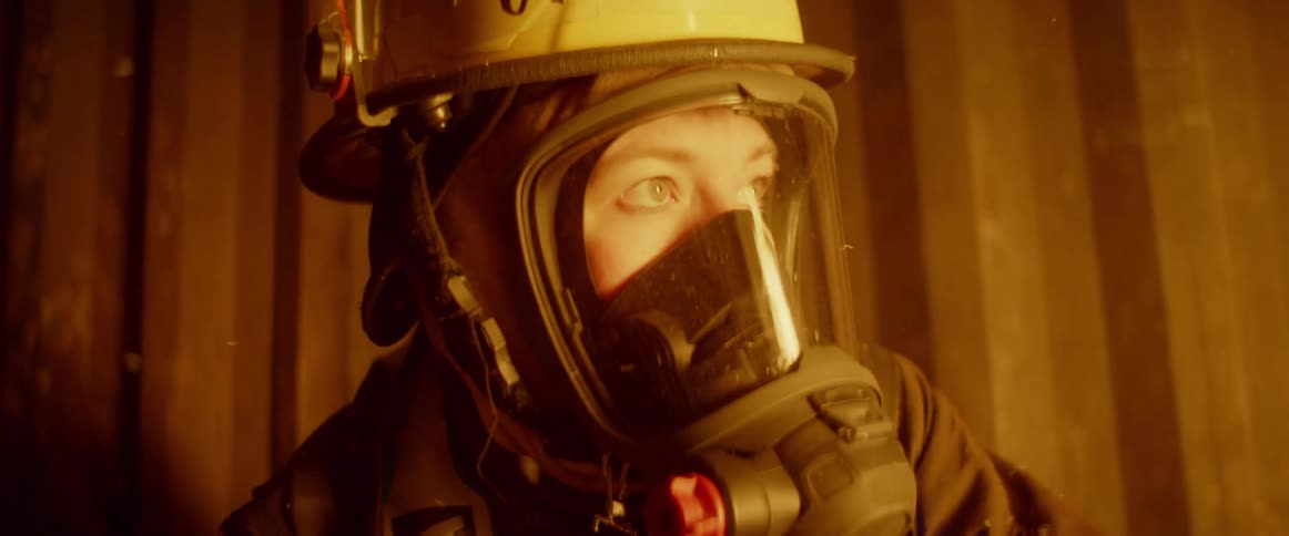 A firefighter looking off into the distance with a fire reflecting off her mask
