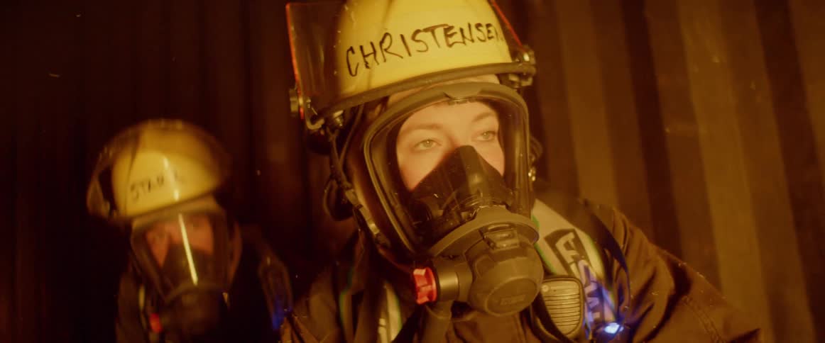 The flames of the fire are reflected on the female firefighters mask and helmet