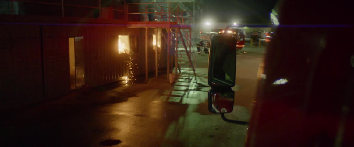 A fire truck drives toward a building with flames shooting out the windows
