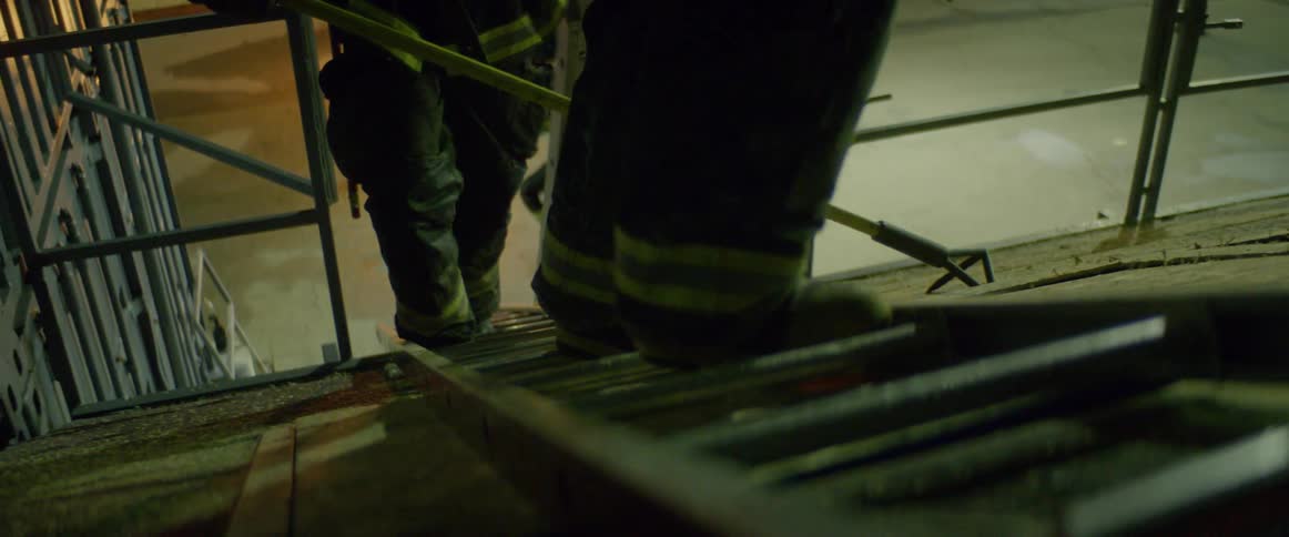 A firefighter pauses and turns as he climbs a ladder on a roof