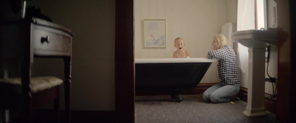A woman blows bubbles at her child in the bathtub