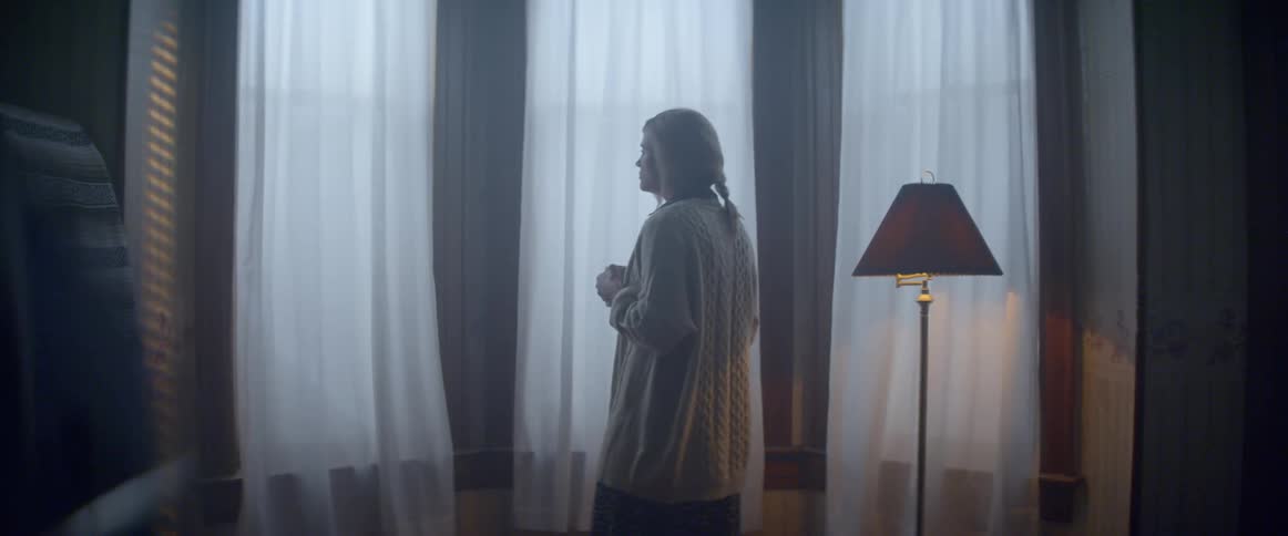 A woman stops to look out large windows in her home