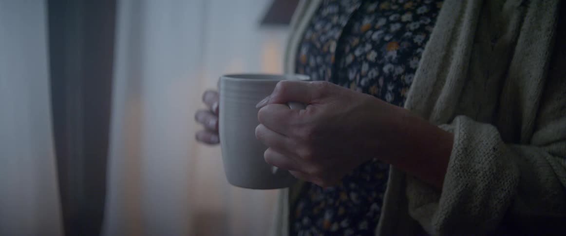 Woman stands in living room holding a cup with hot veberage