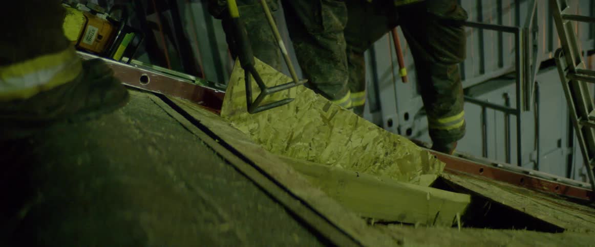 Two firefighters use a tool to break away a roof