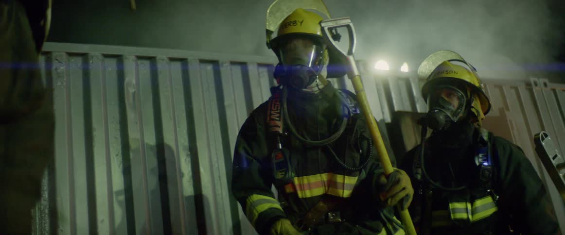 Firefighters holding equipment while standing outside a smoking structure at night