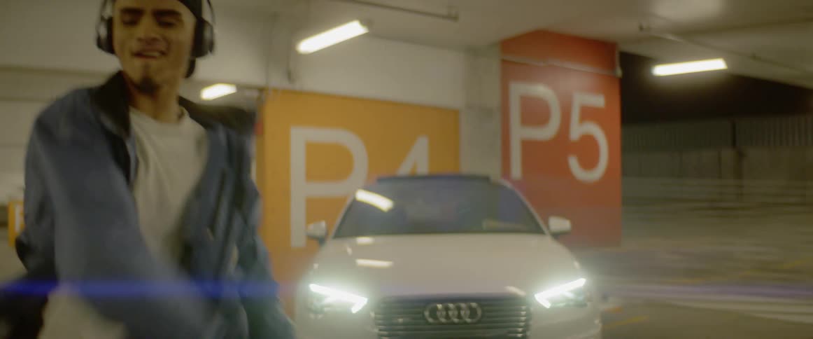 A man dances in front of a car in a parking garage