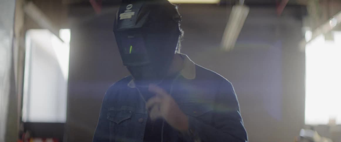 Man walks behind plastic sheeting and puts on welding mask