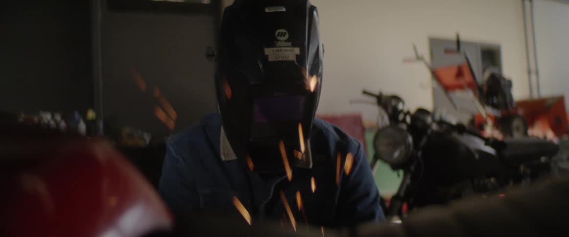 Man wearing uses power tool to work in motorcycle in workshop
