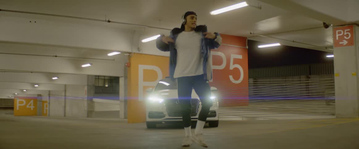 Young man wearing headphones dances in front of car inside parking garage