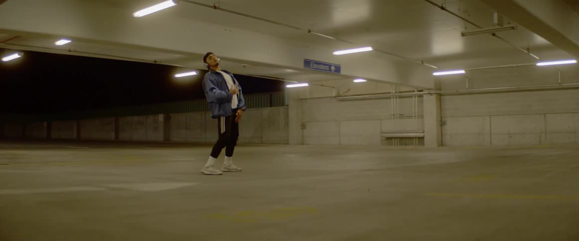 A man wearing headphones dances in an empty parking garage