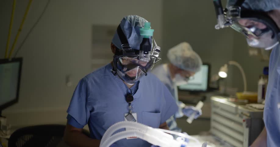 Three people prepare equipment in an operating room