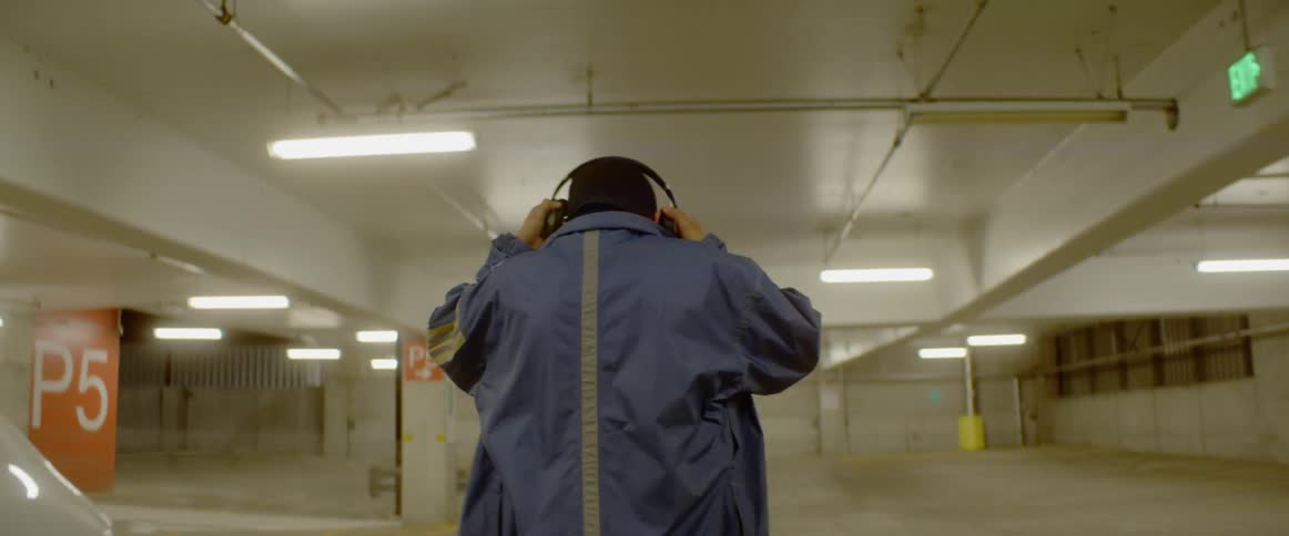 Man gets out of car in parking garage and puts on headphones