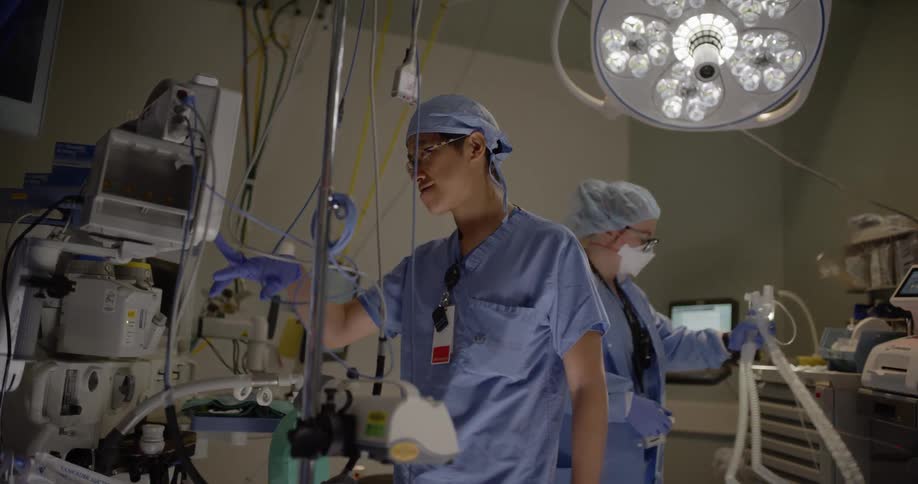 A man adjusts some equipment as a nurse walks behind him