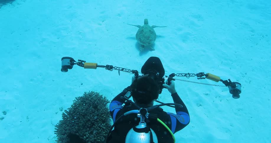 A man is scuba diving while filming a turtle swimming underwater