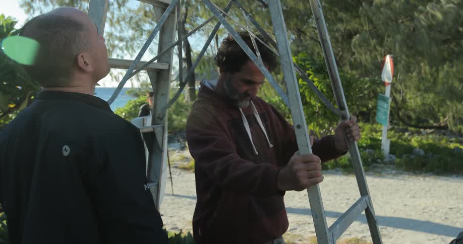 A man sets down a ladder in front of another man