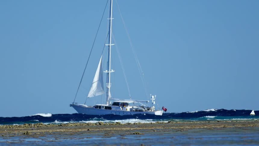 A sailboat bobs on rough waves under a clear sky