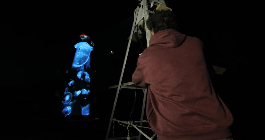Man projecting images onto a lighthouse at night