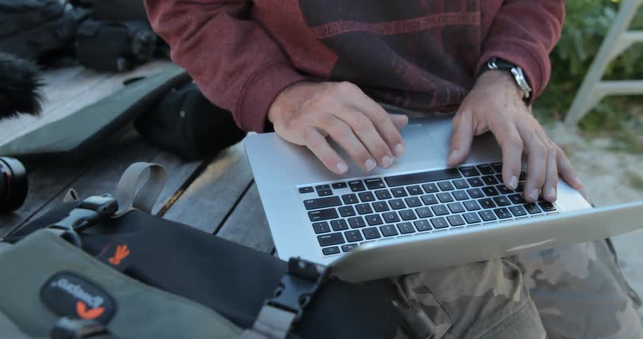 A man works on a laptop while sitting outside