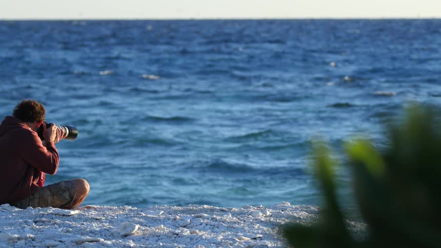 A photographer sits on a sandy beach