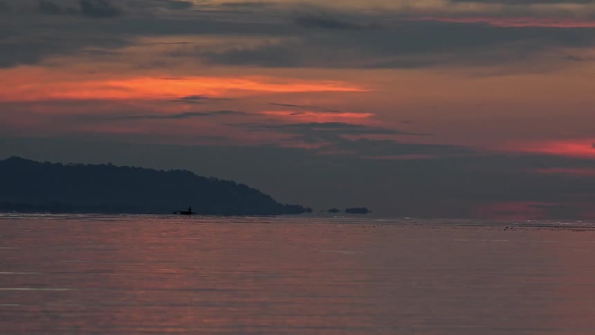 A lone boat makes its way back to shore as the sun sets on a cloudy evening