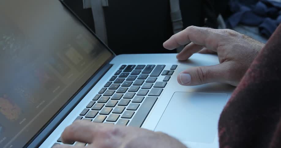 A man balancing a laptop on his lap and scrolling through information on the screen