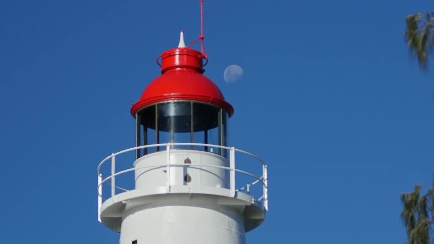 View of a lighthouse tower and a faint moon during daylight
