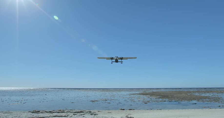 A plane flies low over a beach on a sunny day