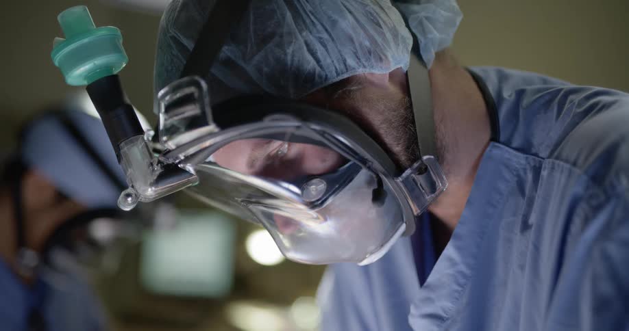 A surgeon walks behind another surgeon in an operating room