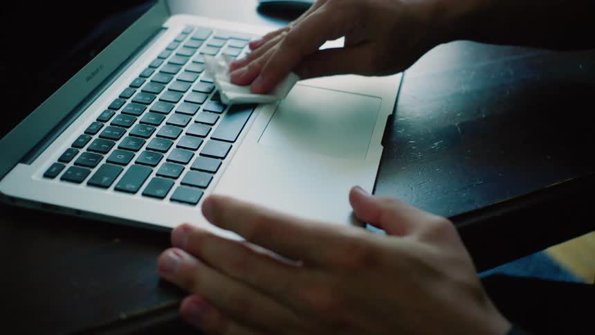 Man cleans laptop keyboard with tissue